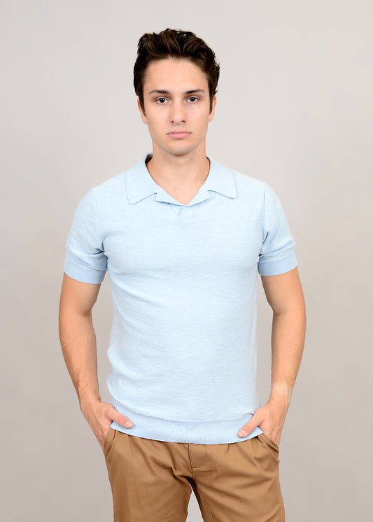 A person with short brown hair wears a light blue Johnny Collar Knit Shirt by HEDGE and beige pants, standing against a plain gray background with hands in pockets.