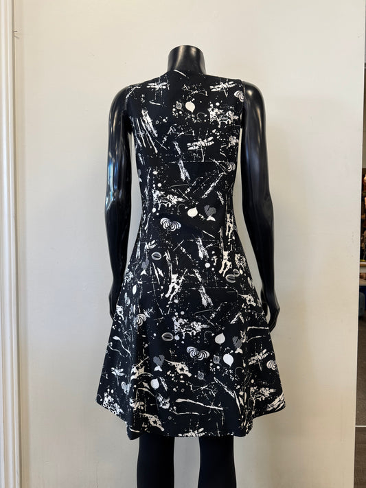 A mannequin showcases Dress 8606 - Bali Corp., sporting a sleeveless black design with white abstract splatters. The dress, by Bali Corp, features a fitted top and subtly flared skirt for comfort. Displayed against a plain white backdrop.