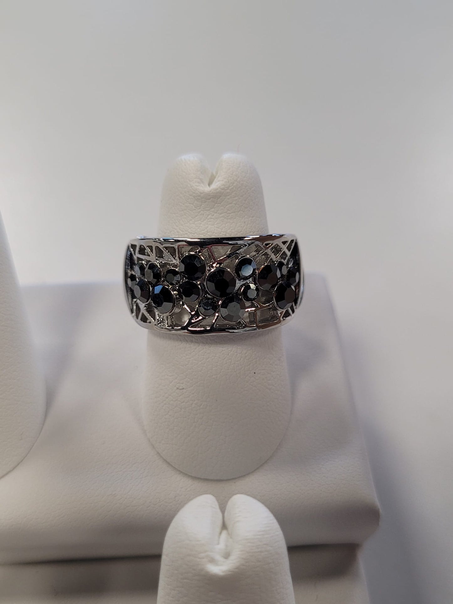 The Jenna-62 Adjustable Ring by Elise Accessories is a stylish piece adorned with multiple black gemstones arranged in a floral pattern. It is beautifully displayed on a white ring stand against a white background.