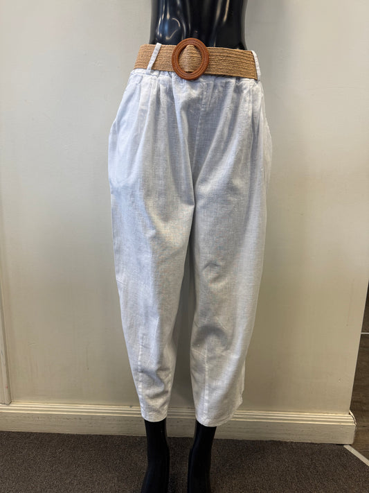 A mannequin displays loose-fitting, light grey Pants with Belt LX38430 by Paolo Tricot, made from a cotton-linen blend for comfort. These high-waisted pants include a tan braided belt with a large circular buckle, set against a simple background of plain walls and carpeted flooring.