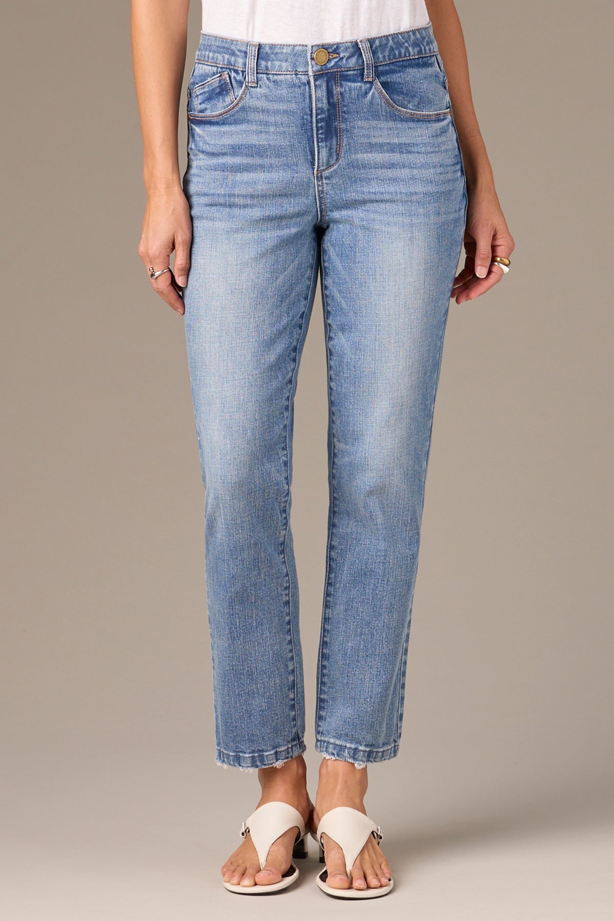 A person wearing Logan Hi-Rise Skinny jeans by Wit & Wisdom in light blue and white sandals stands against a neutral background. The jeans feature a classic five-pocket design, offering a comfortable fit with the hem just above the ankles.