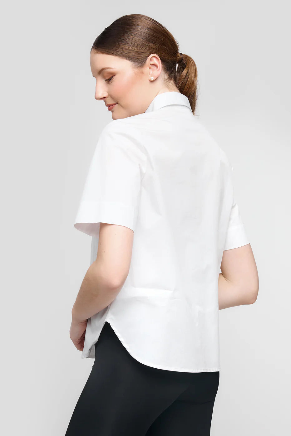 A person with brown hair tied back, in an UCHUU SHORT-SLEEVED SHIRT WITH WAVY RUFFLES CS25-602, and black pants, facing sideways against a gray background.