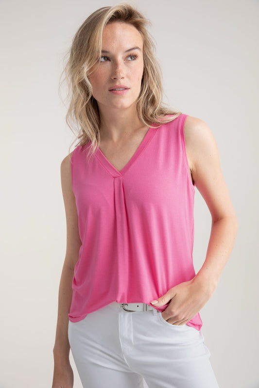 A woman with long blonde hair wears the MARBLE Tank Top Vest 7898 MARBLE and white pants, set against a light gray marble background. She gazes to the side neutrally, her left hand casually in her pocket.