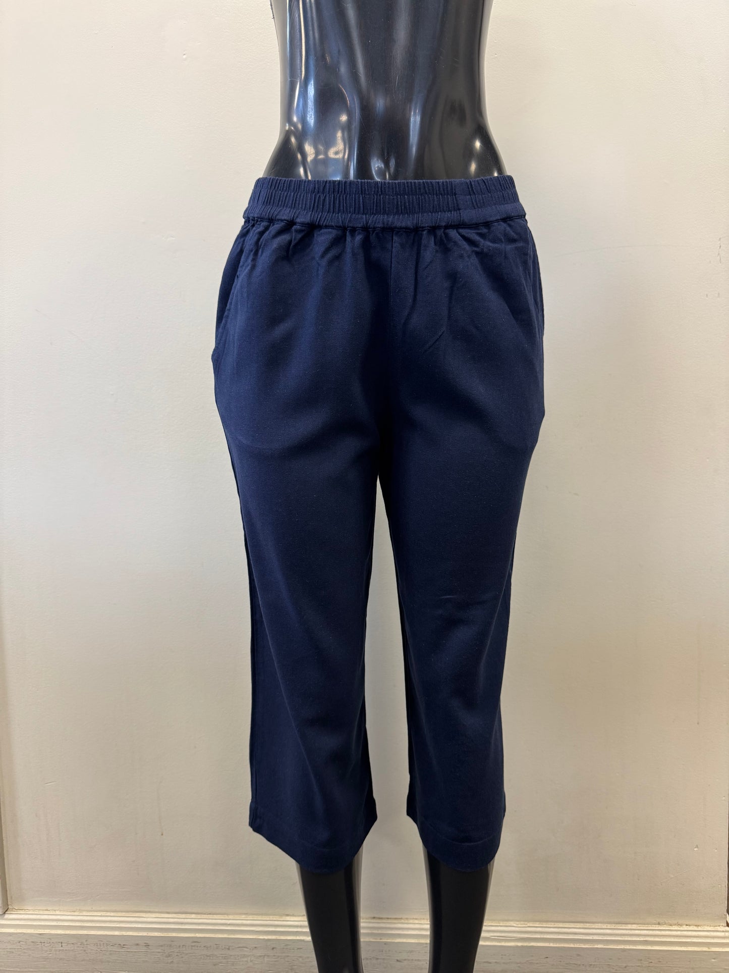 The Pant 6081 by SUNDAY is displayed on a black mannequin, showcasing navy blue cropped pants made from a linen-viscose blend with an elastic waistband, set against a plain pale wall.