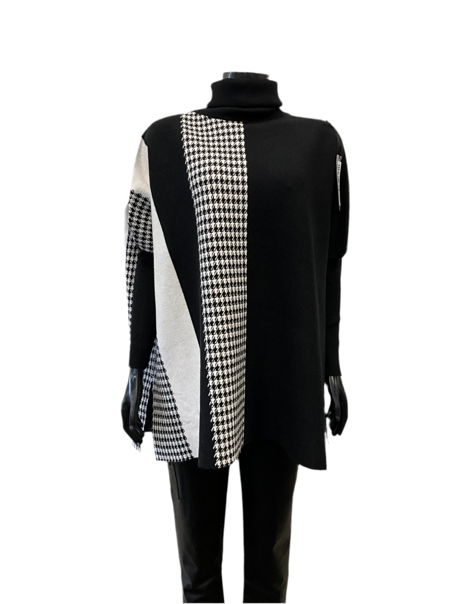 A black long-sleeve turtleneck sweater named "Full Coat Turtle Neck Black - Eternelle" from ETERNELLE, featuring a bold black-and-white geometric pattern with houndstooth and diagonal striped sections on the front. This luxurious top, made in Italy, is paired with black pants and showcased on a mannequin against a white background.