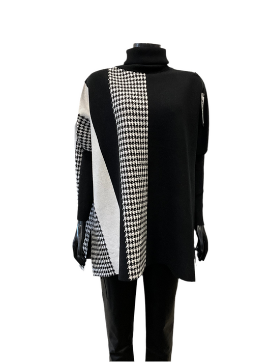 A black long-sleeve turtleneck sweater named "Full Coat Turtle Neck Black - Eternelle" from ETERNELLE, featuring a bold black-and-white geometric pattern with houndstooth and diagonal striped sections on the front. This luxurious top, made in Italy, is paired with black pants and showcased on a mannequin against a white background.