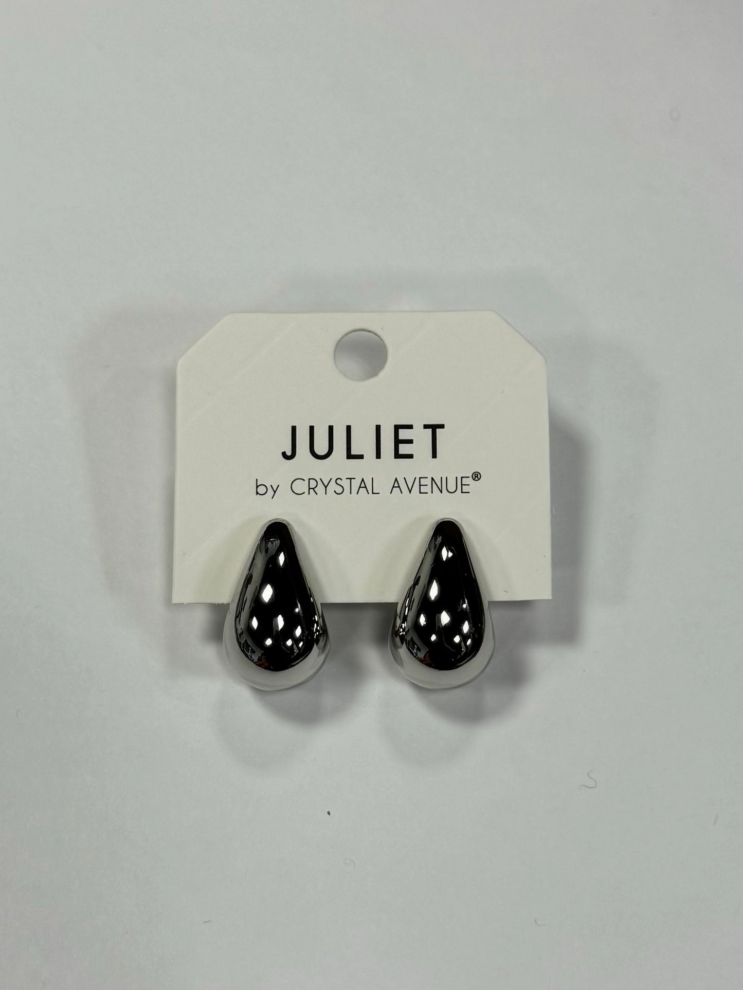 A pair of shiny, silver teardrop-shaped earrings sit on a white card labeled "JULIET by CRYSTAL AVENUE," blending the elegance of Dior Earrings with the charm and style of Elise Accessories from Posies Flowers & Fashion Inc.