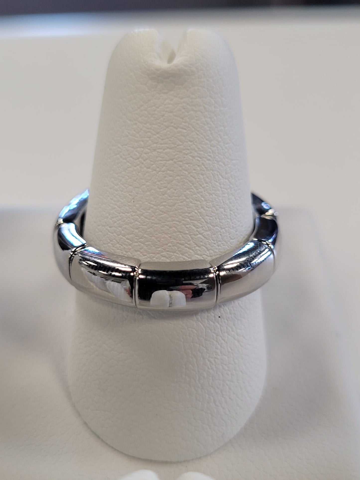 A sleek, modern Jenna-60 Adjustable Ring from Elise Accessories, featuring a CZ solitaire displayed on a textured white ring stand. The silver ring boasts a smooth, chunky band with polished, interconnected segments that provide both structure and style. The background is slightly blurred to draw attention to the ring.
