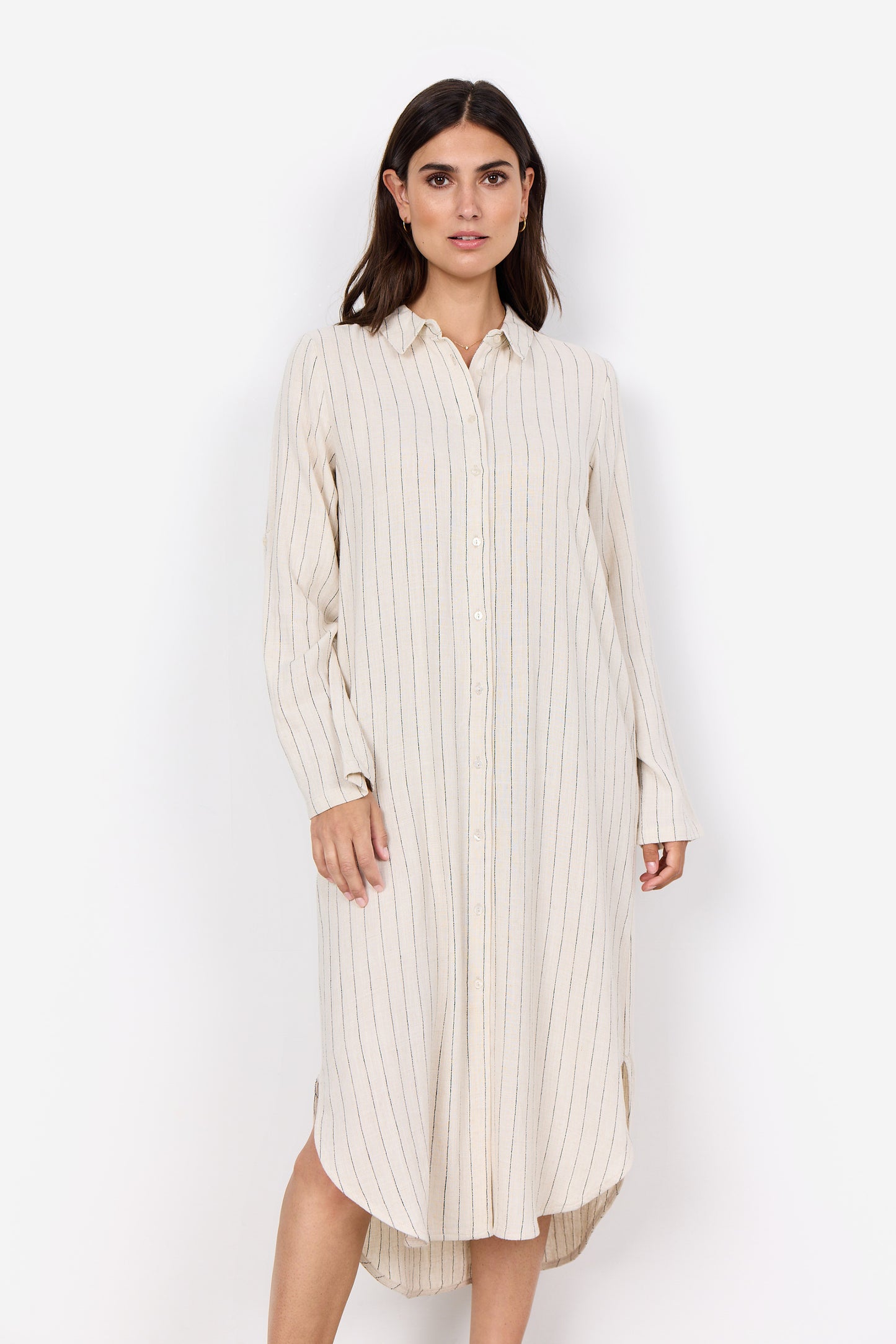 A woman with dark hair stands against a white background, wearing the Poula 4 41090-40 dress by SoyaConcept. The lightweight linen blend piece features thin vertical stripes, long sleeves, a button-down design, and a collar. She looks forward with a neutral expression.