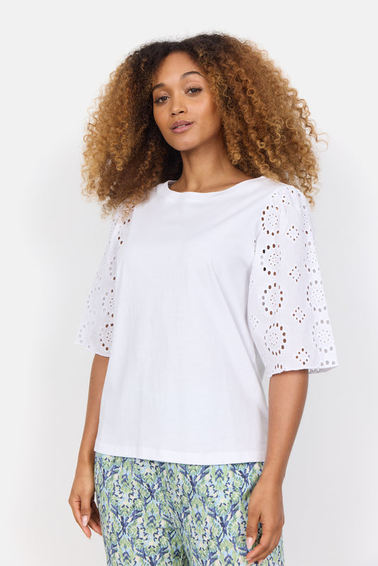 A curly-haired woman wears the stylish Loraine 3 Shirt by SoyaConcept, crafted from organic cotton, paired with patterned pants featuring blue and green floral designs. Neutral background.