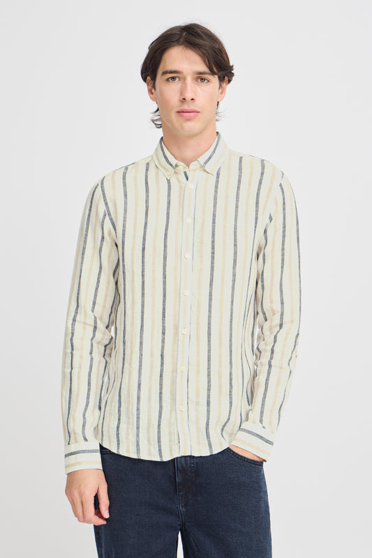 A person with long dark hair is casually dressed for the occasion in a Button Linen Cotton Shirt 20505463 by Casual Fridays, featuring white, beige, and blue vertical stripes. They stand with one hand in their dark jeans pocket against a plain white background.