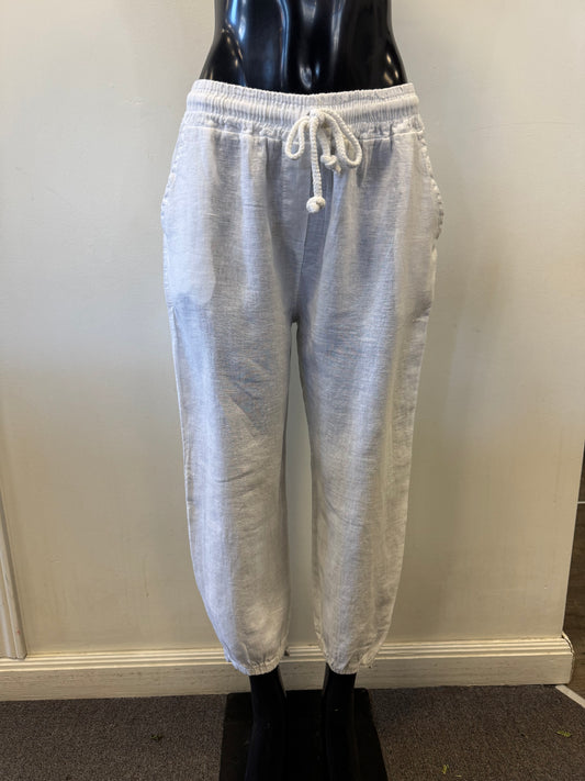 The black mannequin displays Bella Amore's Pants Linen 20836, highlighting designer craftsmanship. Made in Italy, these white pants feature an elastic waistband, side pockets, and ankle cuffs against a plain off-white wall.