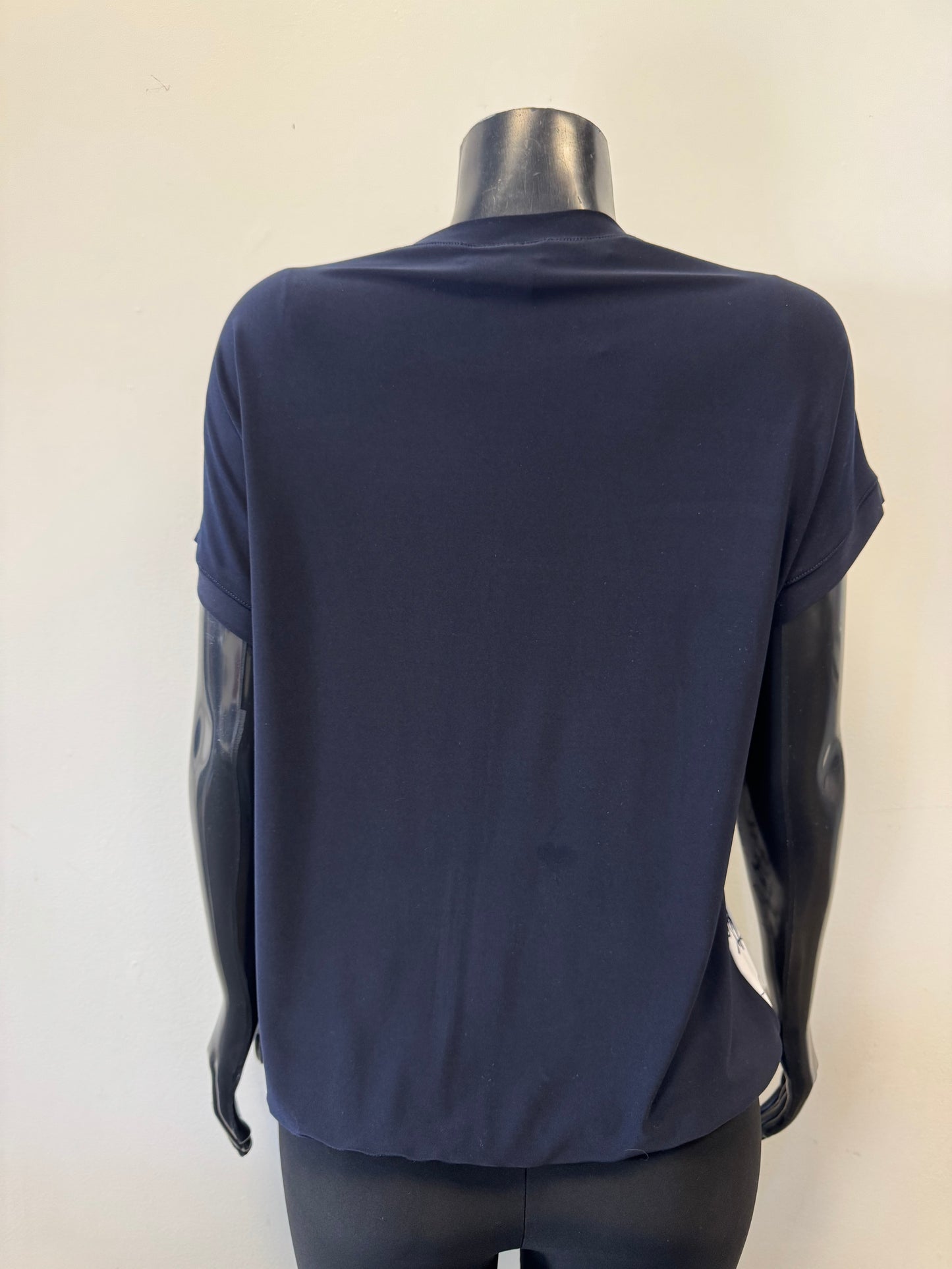 On a mannequin, the dark blue short-sleeve shirt, Top 8547 by Bali Corp., displays a relaxed fit and rolled sleeves. Crafted from a soft polyester blend, it is set against a plain light gray wall.