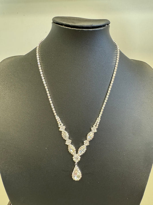 The Avery 1 Necklace and Earring Set by Elise Accessories features a teardrop-shaped pendant with sparkling round and marquise-cut diamonds in a symmetrical design, elegantly displayed on a black stand.