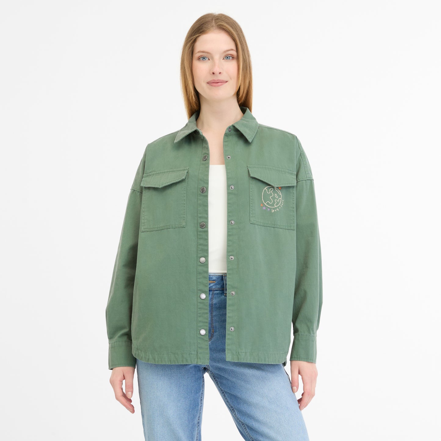 A woman with long hair wears a green button-up LITTA JACKET 2511-60004-5033 from RAGWEAR, featuring two pockets and a white graphic. She combines it with a light green top, blue jeans, and stands against a plain white background.