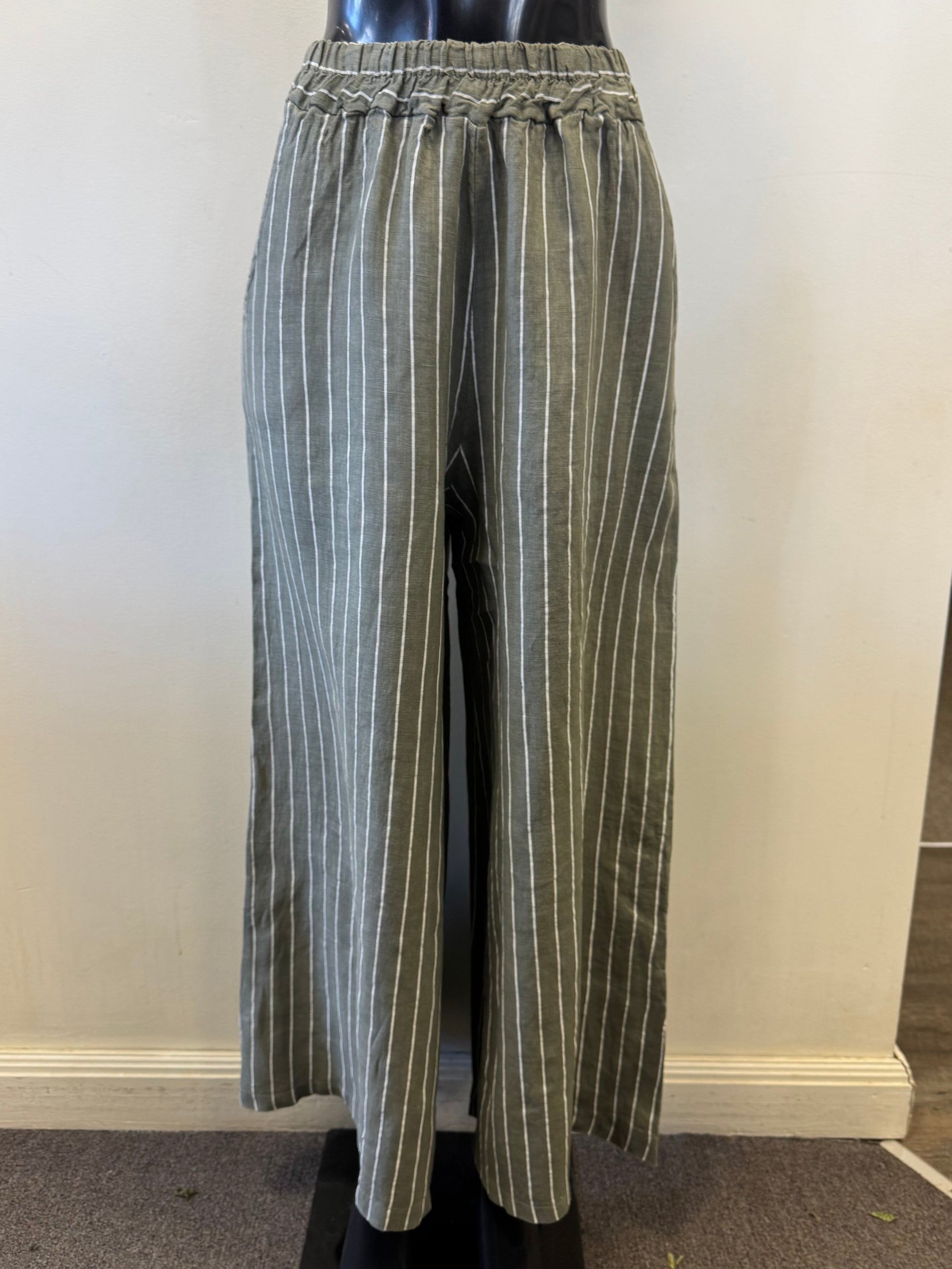 Bella Amore showcases Linen Pants 1045, gray wide-leg pants with green and white stripes, on a mannequin. These pants have an elastic waistband and a loose fit, set against a light-colored wall and carpeted floor.