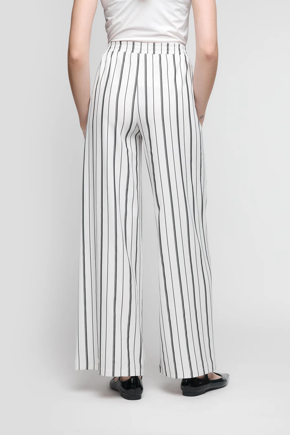 A person is seen from behind wearing UCHUU's CS25-112 pants with black and white stripes, paired with a white top and black shoes against a light gray backdrop.