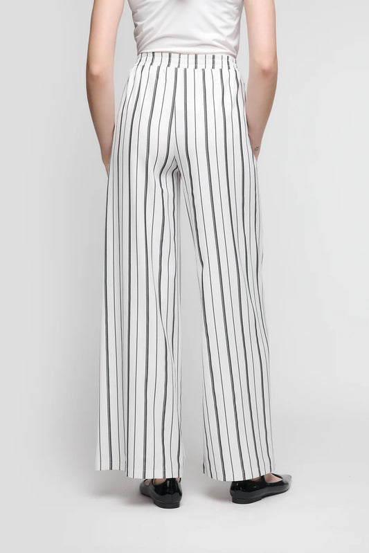 A person is seen from behind wearing UCHUU's CS25-112 pants with black and white stripes, paired with a white top and black shoes against a light gray backdrop.