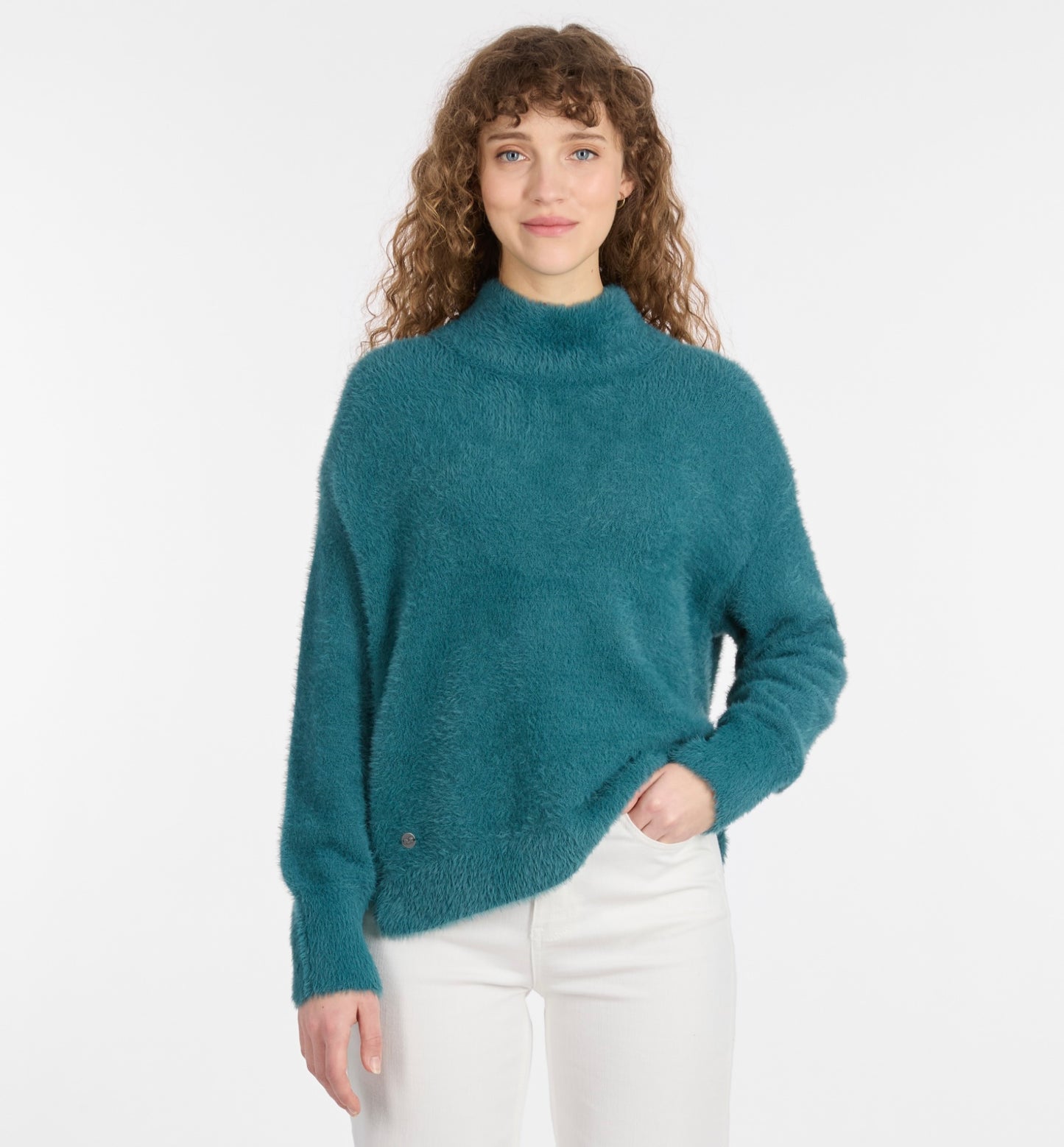 A woman with curly brown hair softly smiles at the camera while wearing the RAGWEAR YESSIE Flat Knit Sweater and white pants, standing against a plain white background.