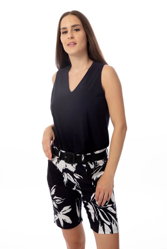 A person with long brown hair wears the versatile Bali Corp's Bali Top Sleeveless 8326 in black, paired with black and white floral shorts. They stand against a white background, exuding a relaxed vibe with one hand on their hip.