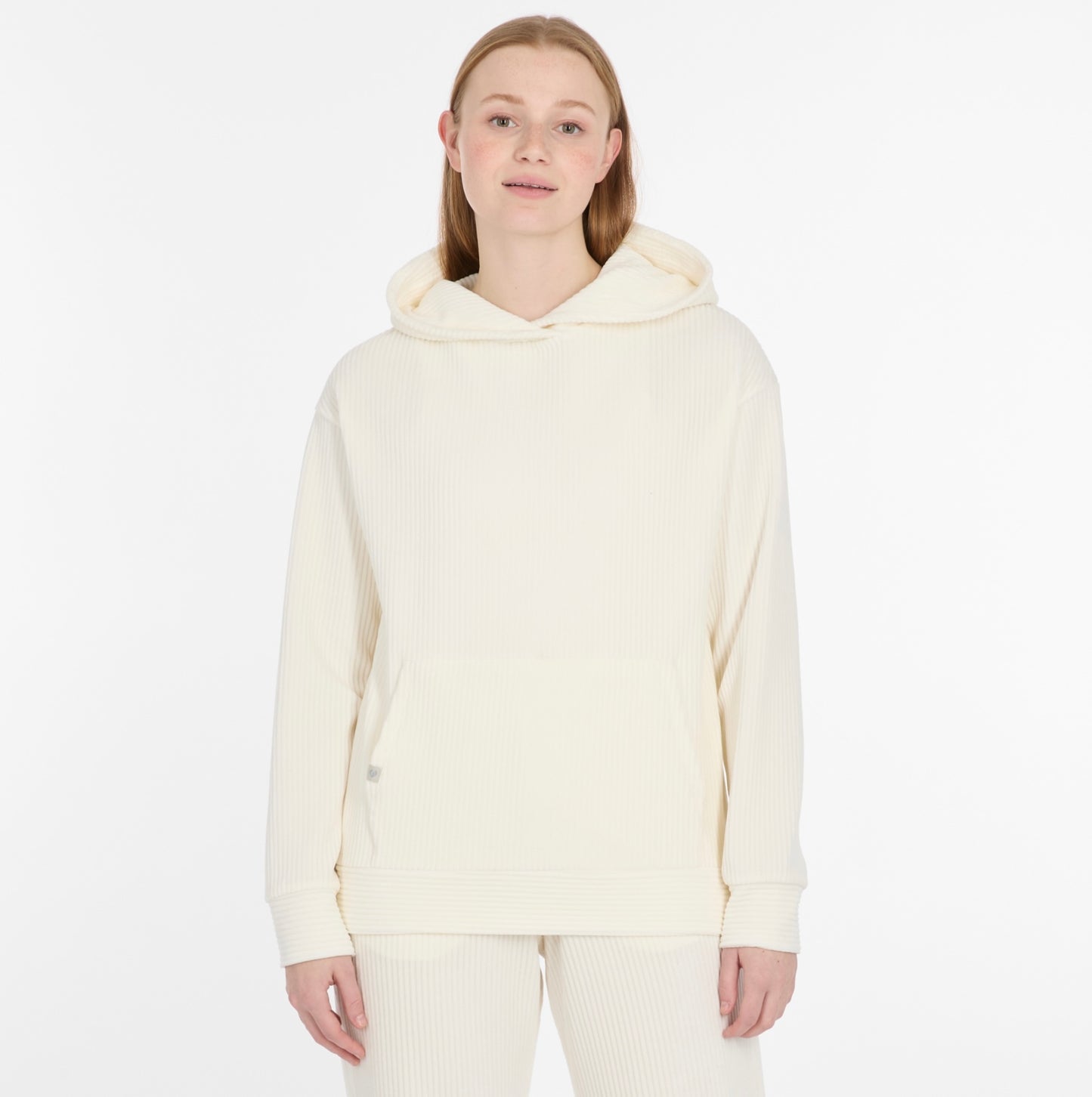 A person with straight blonde hair wears a cozy, off-white COLBIE CORDY Sweatshirt by RAGWEAR with matching pants, standing against a plain white background and smiling gently at the camera.