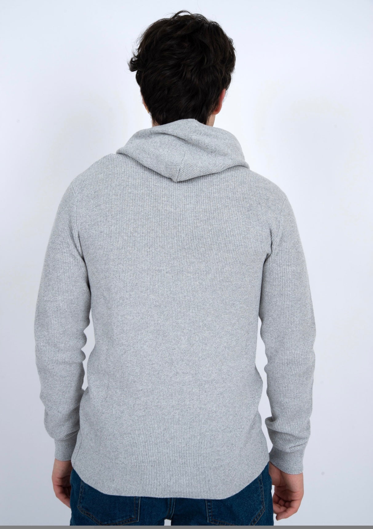 A person with dark hair, wearing HEDGE’s eco-friendly MENS HOODED SWEATER-OATMEAL MEL TWIST and blue jeans, stands with their back to the camera against a plain white background.