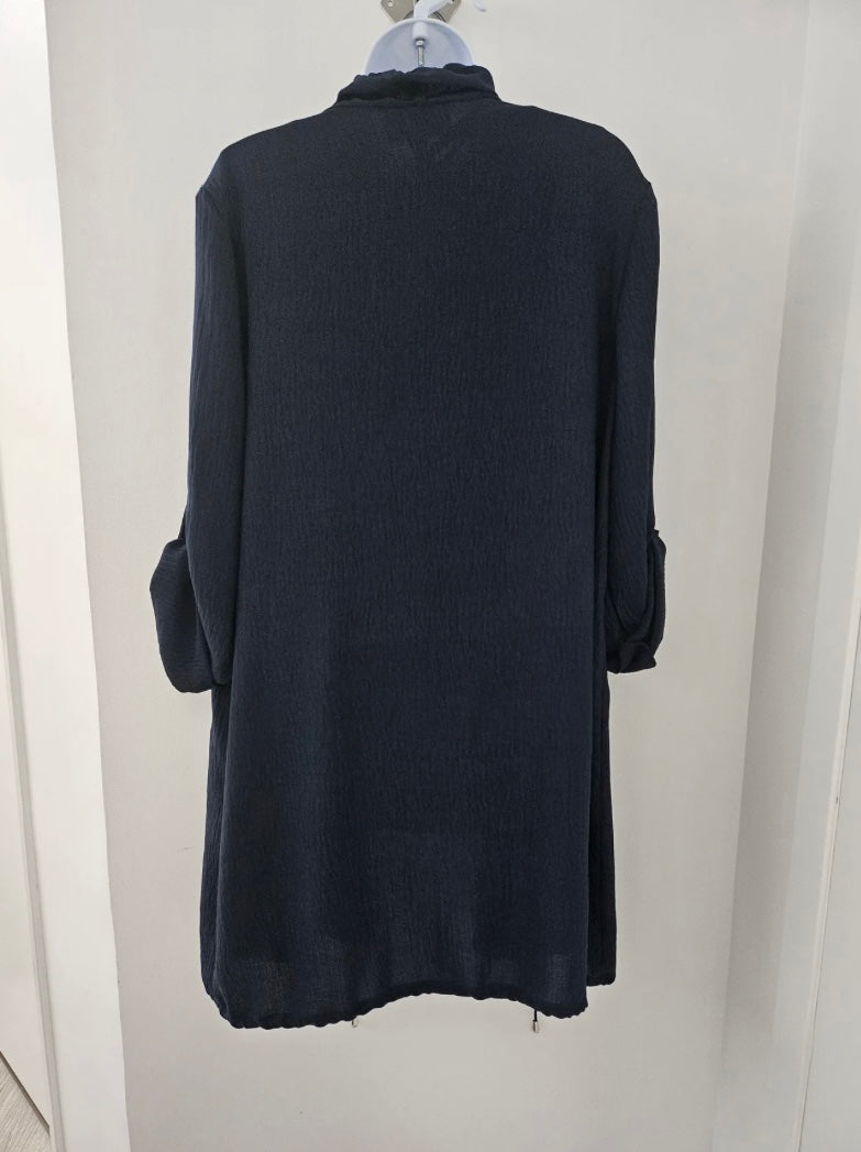 A navy Joseph Ribkoff - Gauze Boxy Cover Up MIDNIGHT BLUE 242058 with long sleeves and silver button details hangs on a mannequin, highlighted by a shawl collar for added elegance. The mannequin wears a white top underneath the cover up. The ensemble is set against a plain, light-colored wall.