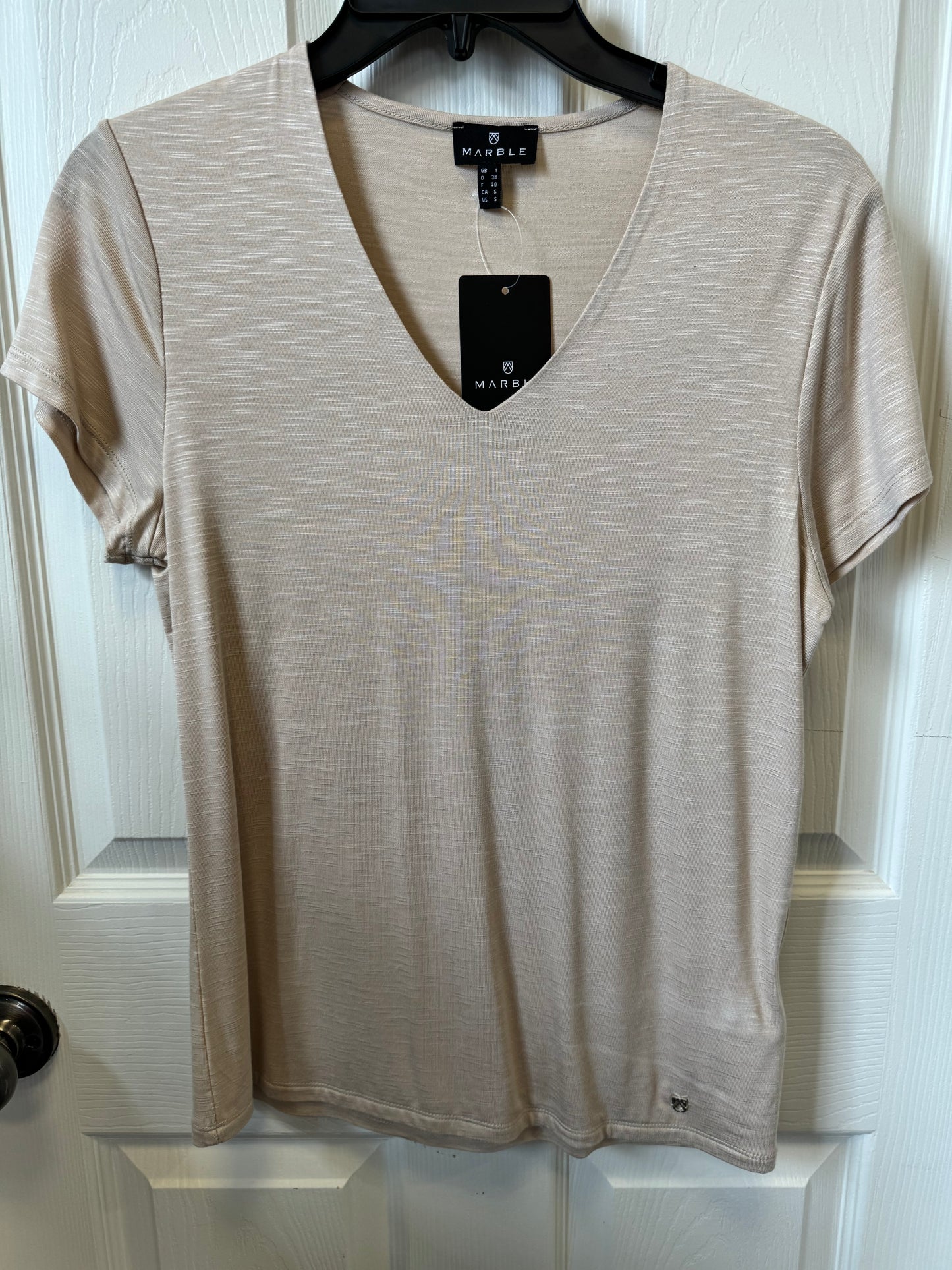 A Marble Fitted V-Neck T-Shirt - BEIGE 6539 is displayed on a black hanger against a white door. The shirt has a fitted silhouette, subtle marbled texture, and features a black rectangular tag with the brand name "MARBLE," along with a smaller label on the left bottom hem.