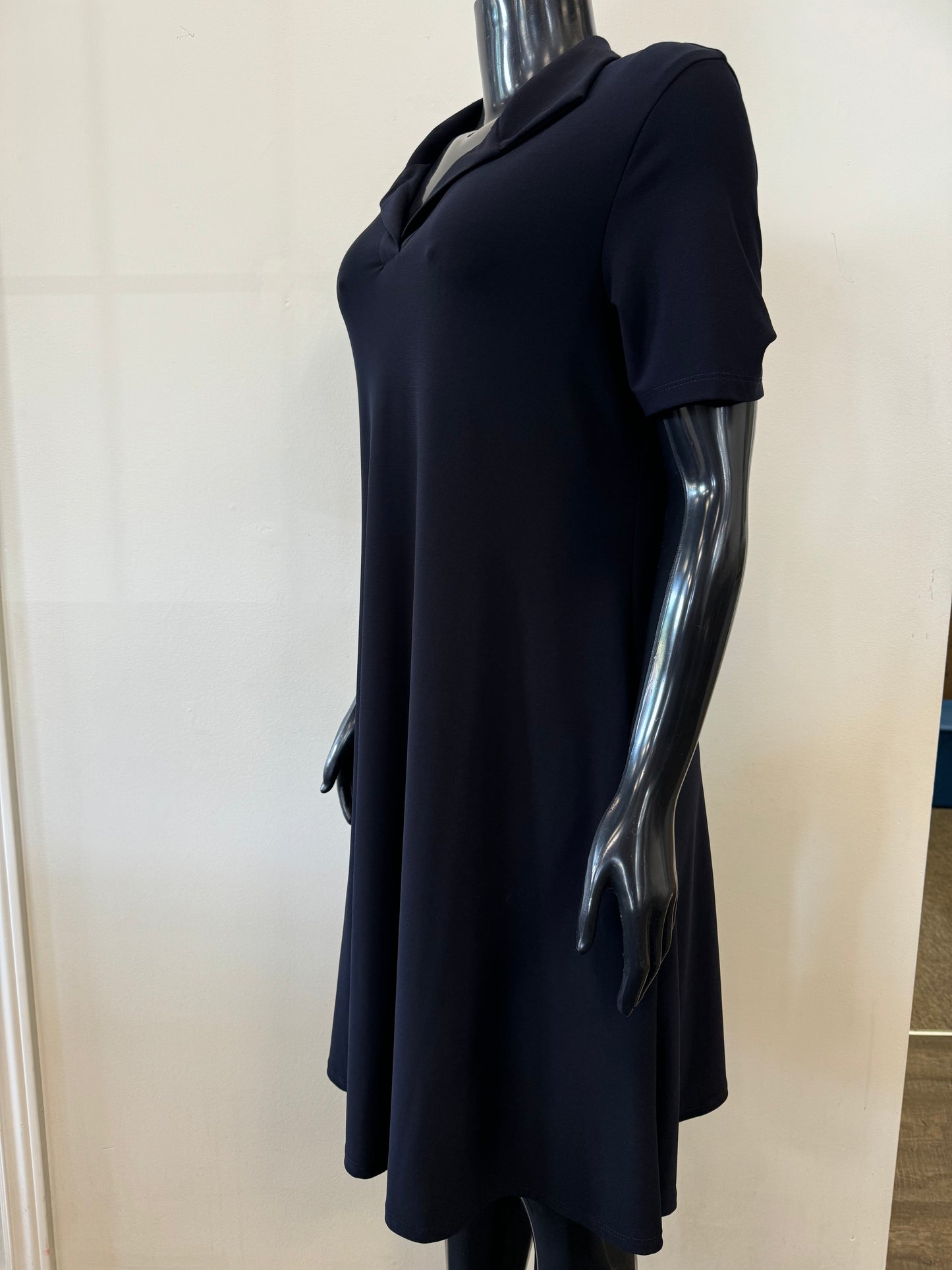 A black mannequin dressed in Bali Corp's Navy Dress 8031, featuring a knee-length, short-sleeve design with a V-neckline and a slightly flared skirt. The mannequin stands against a plain, light-colored background.