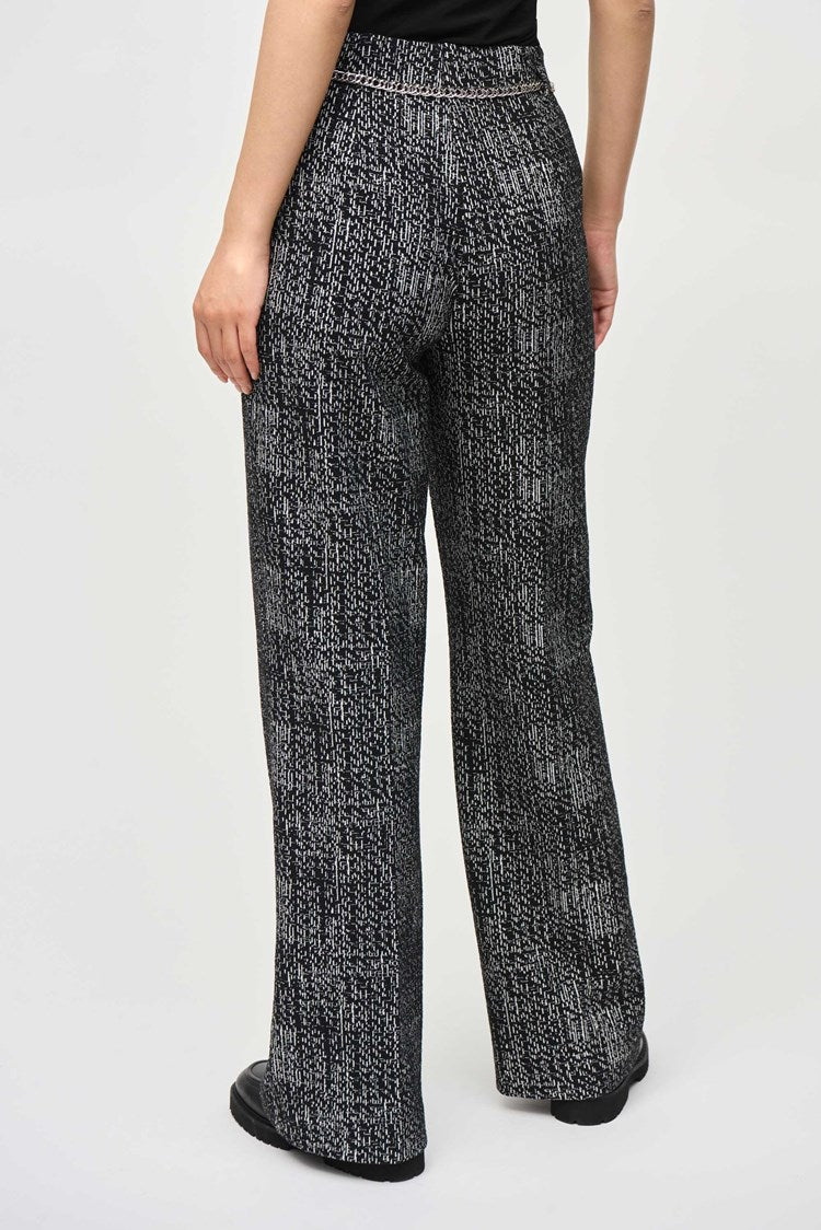 A person with long, straight black hair and bangs stands against a plain background. They are wearing a black and white patterned tweed knit fabric blazer with matching wide-leg pants, specifically Tweed Knit Wide-Leg Pull-On Pants 243288 by Joseph Ribkoff, and black shoes. They have an expressionless face, and their hands are relaxed by their sides.