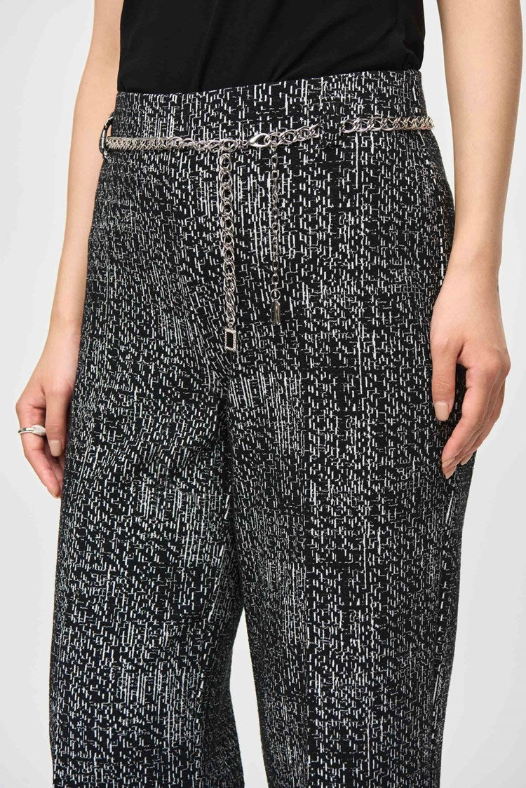 A person with long, straight black hair and bangs stands against a plain background. They are wearing a black and white patterned tweed knit fabric blazer with matching wide-leg pants, specifically Tweed Knit Wide-Leg Pull-On Pants 243288 by Joseph Ribkoff, and black shoes. They have an expressionless face, and their hands are relaxed by their sides.