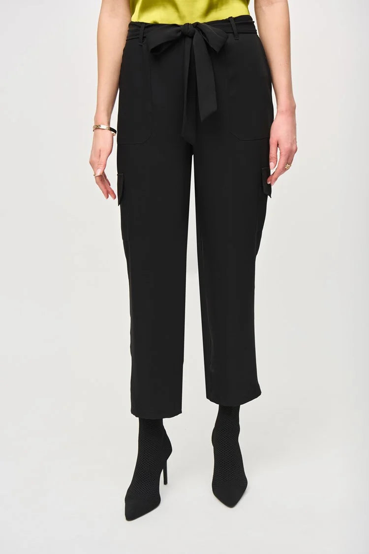 A woman stands against a plain white background, wearing a short-sleeve, lime green blouse paired with the Stretch Woven Pull-On Cargo Pants 243077 by Joseph Ribkoff. The high-waisted, black cropped pants feature a tied belt at the waist. She completes her look with black ankle boots. Her blonde hair is styled in loose waves and she has neutral makeup.