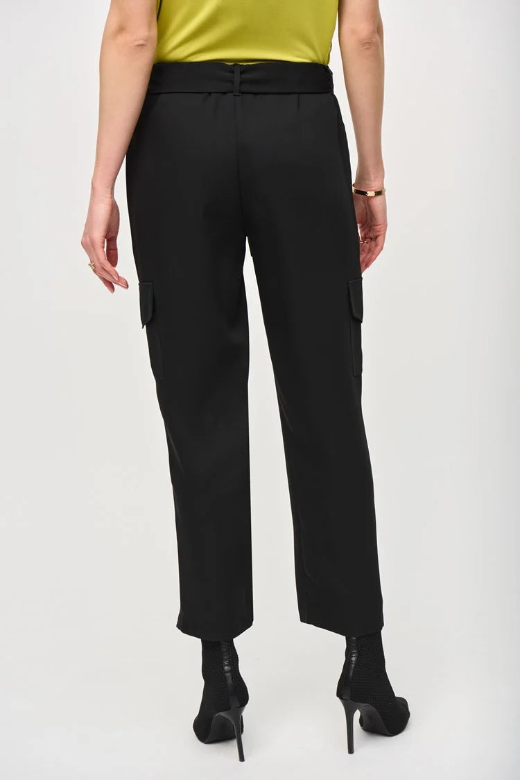 A woman stands against a plain white background, wearing a short-sleeve, lime green blouse paired with the Stretch Woven Pull-On Cargo Pants 243077 by Joseph Ribkoff. The high-waisted, black cropped pants feature a tied belt at the waist. She completes her look with black ankle boots. Her blonde hair is styled in loose waves and she has neutral makeup.