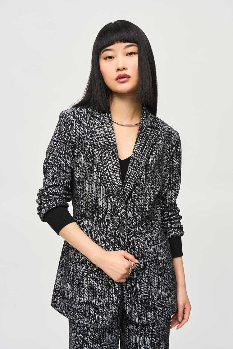 A person with long, straight hair stands against a plain backdrop wearing a matching dark patterned Joseph Ribkoff Tweed Knit Fitted Blazer (243053) and wide-leg pants with a textured design, embodying the elegance of a versatile fashion piece. Their hands are relaxed at their sides as they look slightly to the left with a neutral expression.