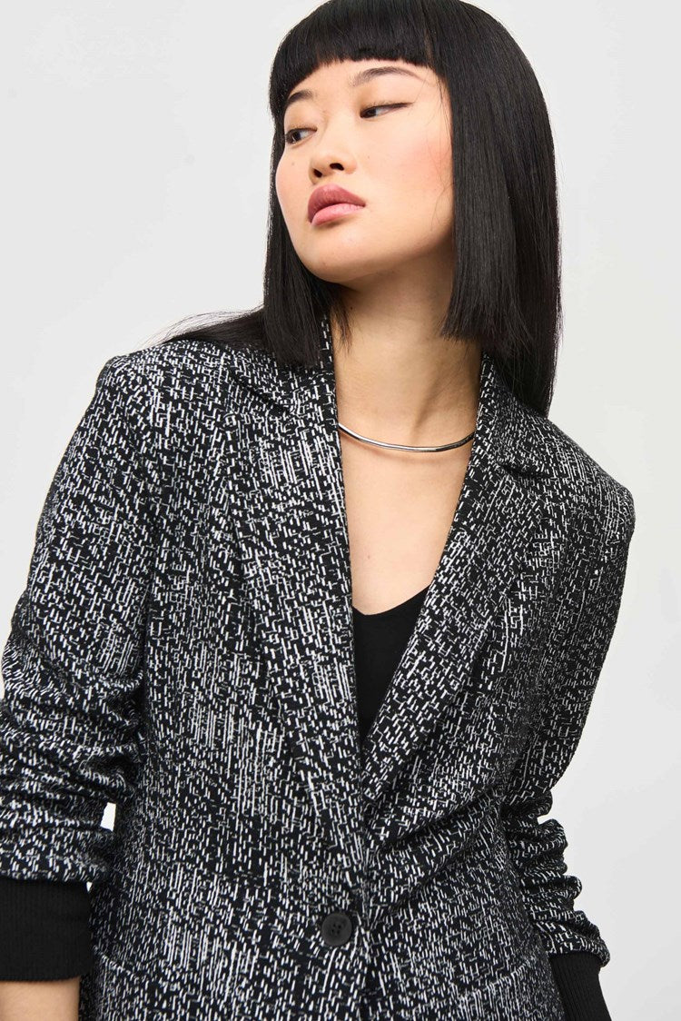 A person with long, straight hair stands against a plain backdrop wearing a matching dark patterned Joseph Ribkoff Tweed Knit Fitted Blazer (243053) and wide-leg pants with a textured design, embodying the elegance of a versatile fashion piece. Their hands are relaxed at their sides as they look slightly to the left with a neutral expression.