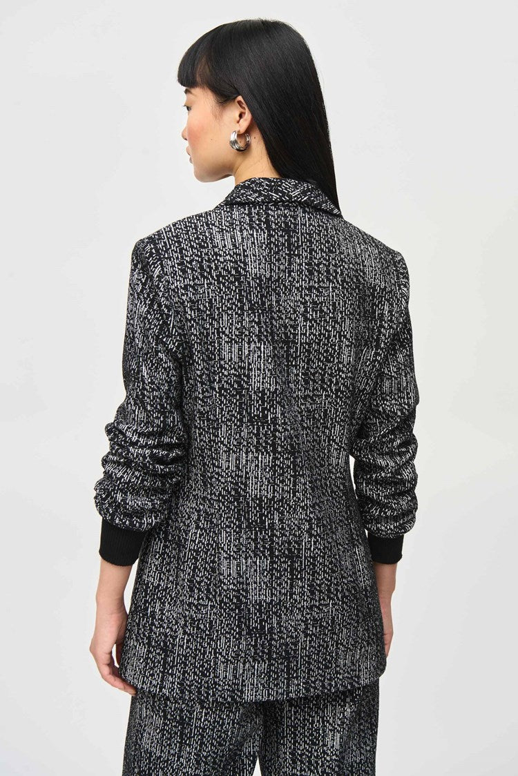 A person with long, straight hair stands against a plain backdrop wearing a matching dark patterned Joseph Ribkoff Tweed Knit Fitted Blazer (243053) and wide-leg pants with a textured design, embodying the elegance of a versatile fashion piece. Their hands are relaxed at their sides as they look slightly to the left with a neutral expression.