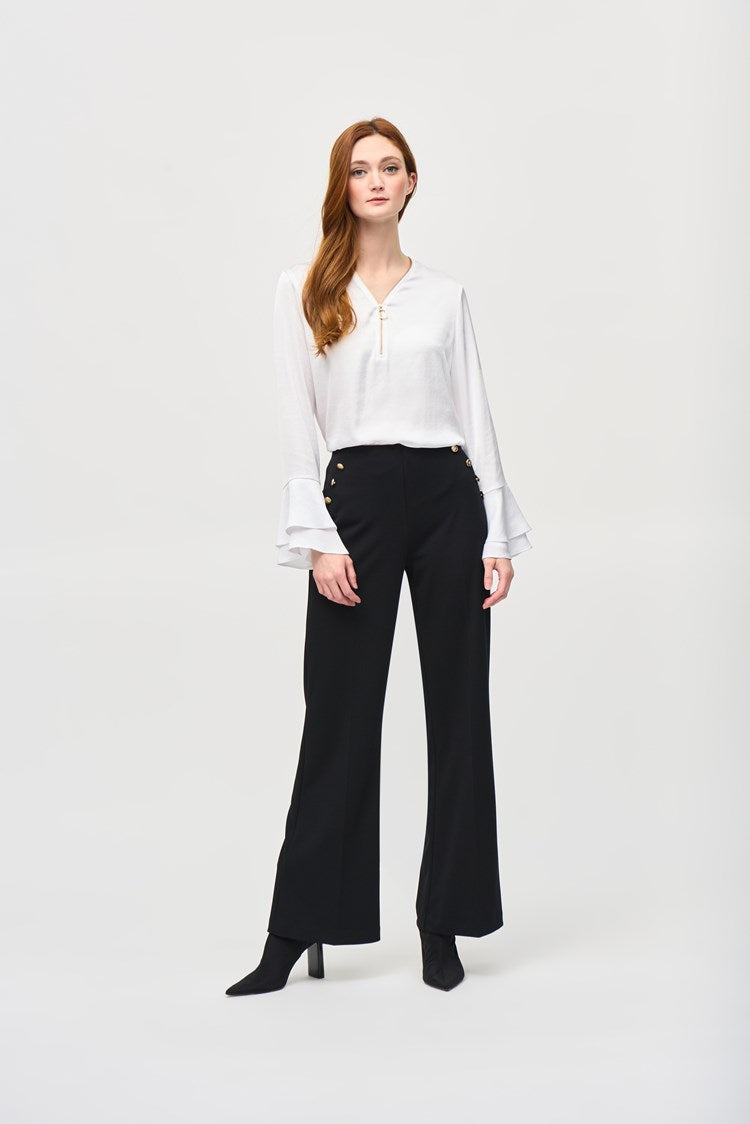 A woman with long reddish-brown hair wearing the Joseph Ribkoff Satin Boxy Top With Ruffled Sleeve 243285, which features a V-shaped neckline and long ruffled sleeves, stands against a plain white background. She is looking directly at the camera with a neutral expression, one hand by her side and the other resting on her hip.