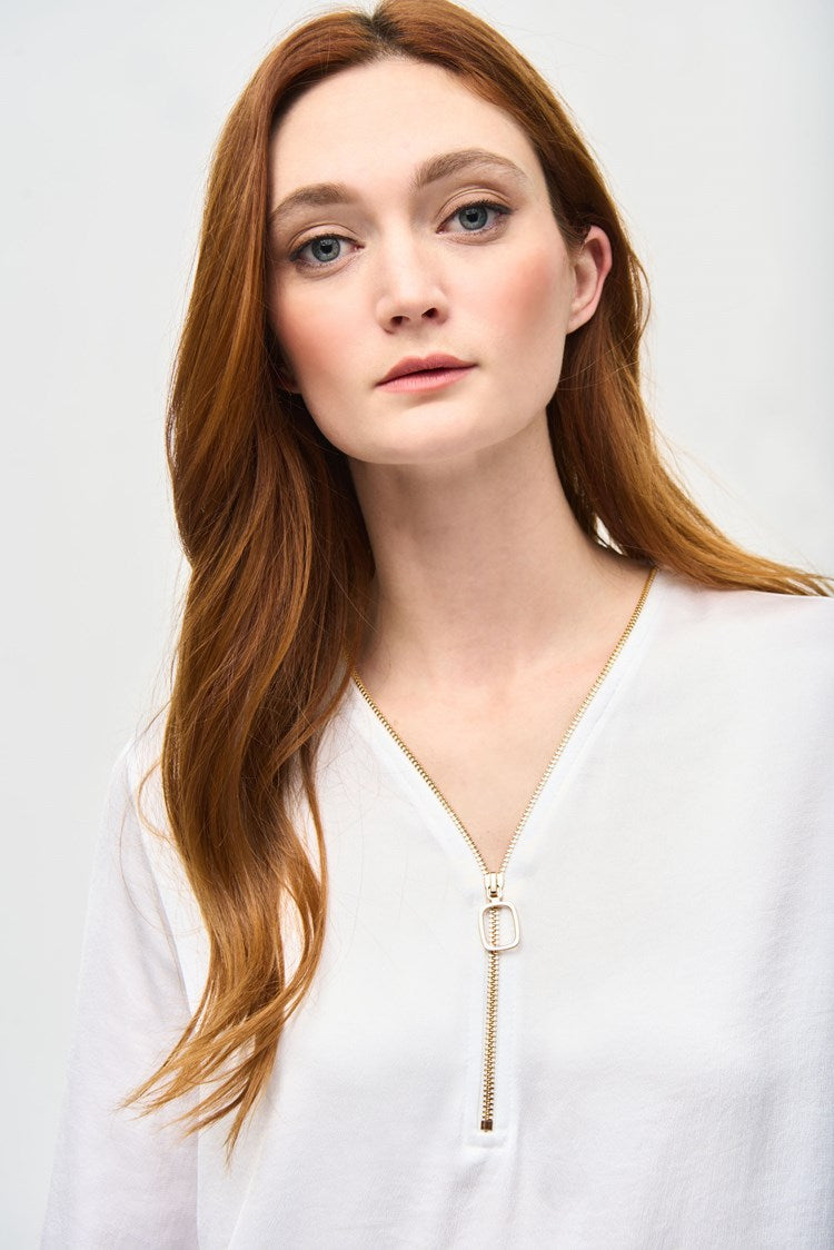 A woman with long reddish-brown hair wearing the Joseph Ribkoff Satin Boxy Top With Ruffled Sleeve 243285, which features a V-shaped neckline and long ruffled sleeves, stands against a plain white background. She is looking directly at the camera with a neutral expression, one hand by her side and the other resting on her hip.