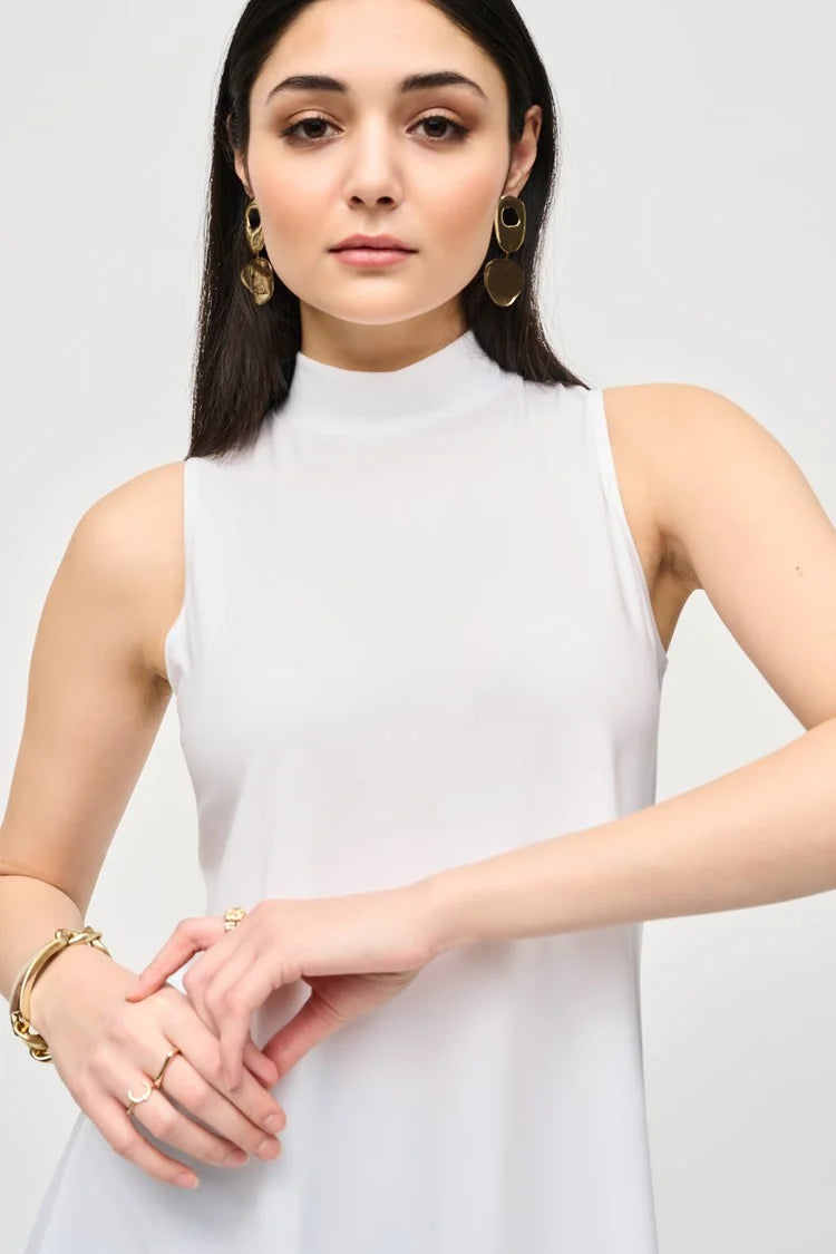 A woman with long dark hair stands against a plain background. She is wearing a Joseph Ribkoff Silky Knit Fit and Flare Sleeveless Top 243253, black flared pants, and black ankle boots. She has minimal jewelry and is striking a relaxed, confident pose with a slight smile.