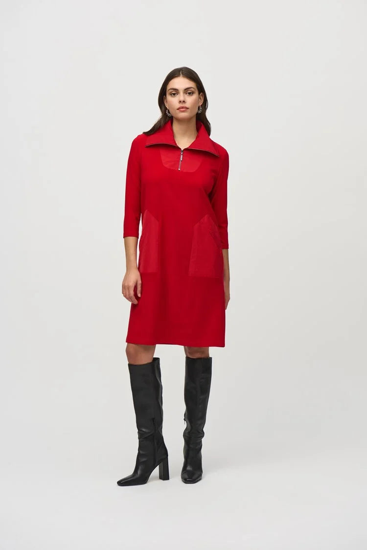 A woman with long dark hair wears the Silky Knit And Memory Straight Dress 244045 by Joseph Ribkoff, a knee-length dress with an A-line silhouette in red bouclé mesh fabric. The dress features a zipped neckline and quarter sleeves. She stands against a plain background, one hand raised to her head as she looks down to the left. Black knee-high boots complete her look.