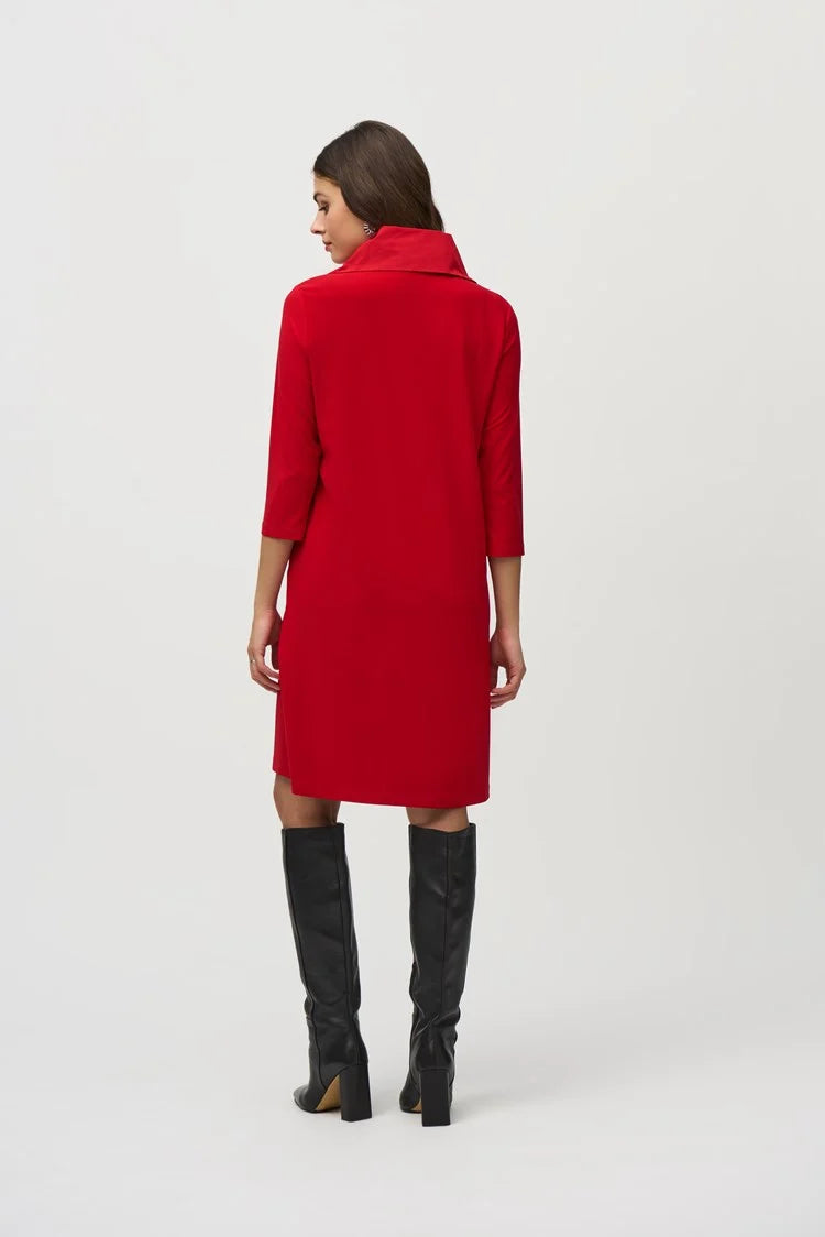 A woman with long dark hair wears the Silky Knit And Memory Straight Dress 244045 by Joseph Ribkoff, a knee-length dress with an A-line silhouette in red bouclé mesh fabric. The dress features a zipped neckline and quarter sleeves. She stands against a plain background, one hand raised to her head as she looks down to the left. Black knee-high boots complete her look.