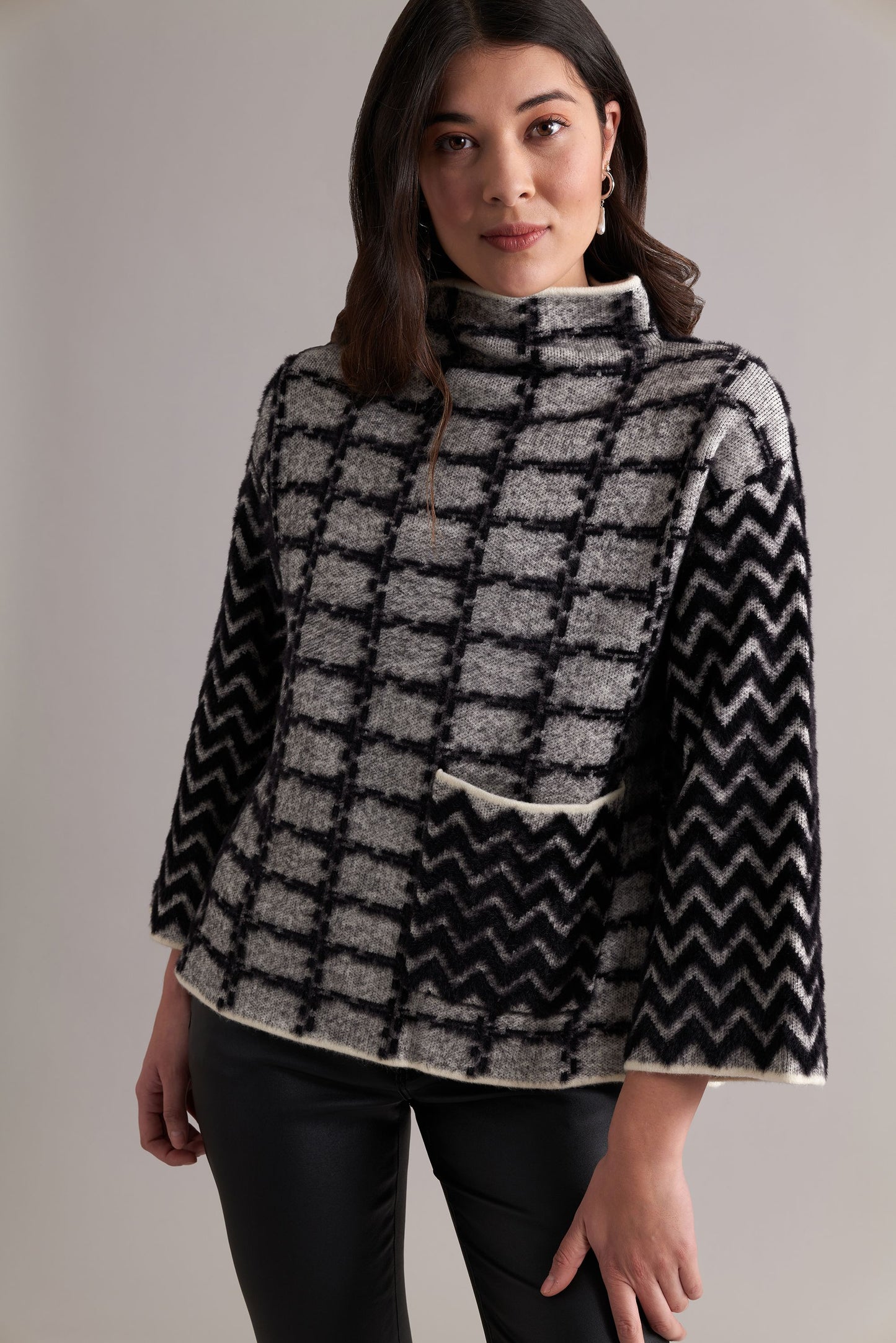 A person with long, dark hair is wearing the FOIL Game Of Thrones Sweater, which features a high-neck and black and white checkered pattern with chevron-patterned sleeves. They have their arms slightly raised and appear to be in motion, standing against a plain background.