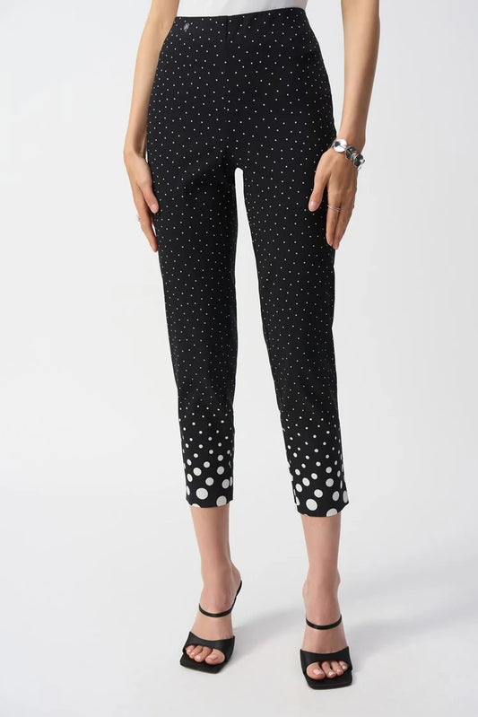 A person stands against a white background in Joseph Ribkoff's Millennium Dot Print Straight Pants, featuring larger dots near the ankles. They pair it with black open-toe heels and a silver bracelet for a sleek look.