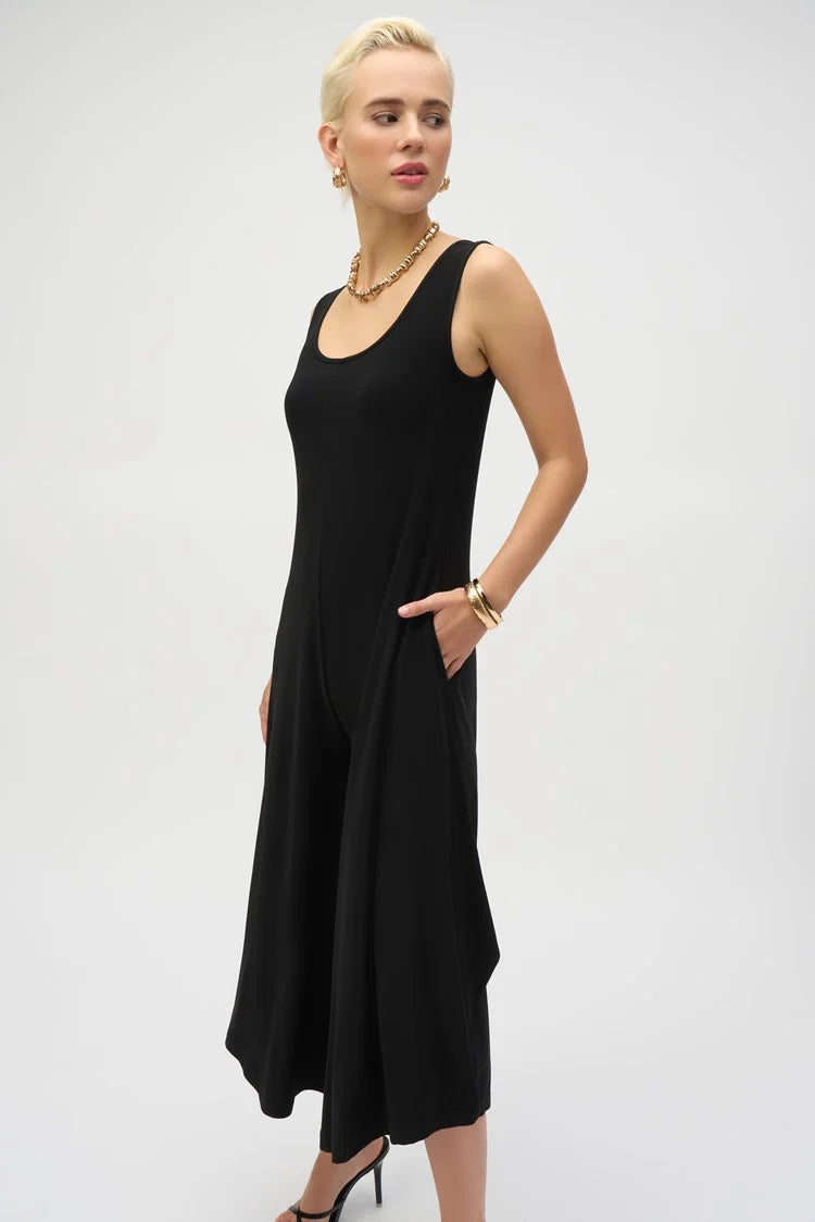 A person in a Joseph Ribkoff Silky Knit Wide-Leg Sleeveless Jumpsuit 252056 poses with short blond hair, accessorized with gold hoop earrings, a necklace, a bracelet, and black heels against a plain background.