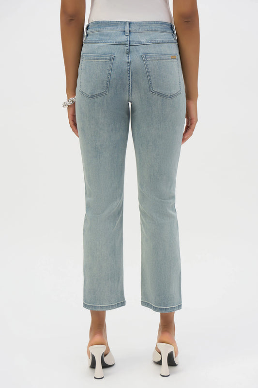 Rear view of a person in Joseph Ribkoff's Margot Classic Straight Leg Stretch Jeans, crafted from Featherweave denim, paired with white heeled shoes. The light blue jeans have two back pockets and a vintage wash charm. A bracelet graces their right wrist against a plain white backdrop.