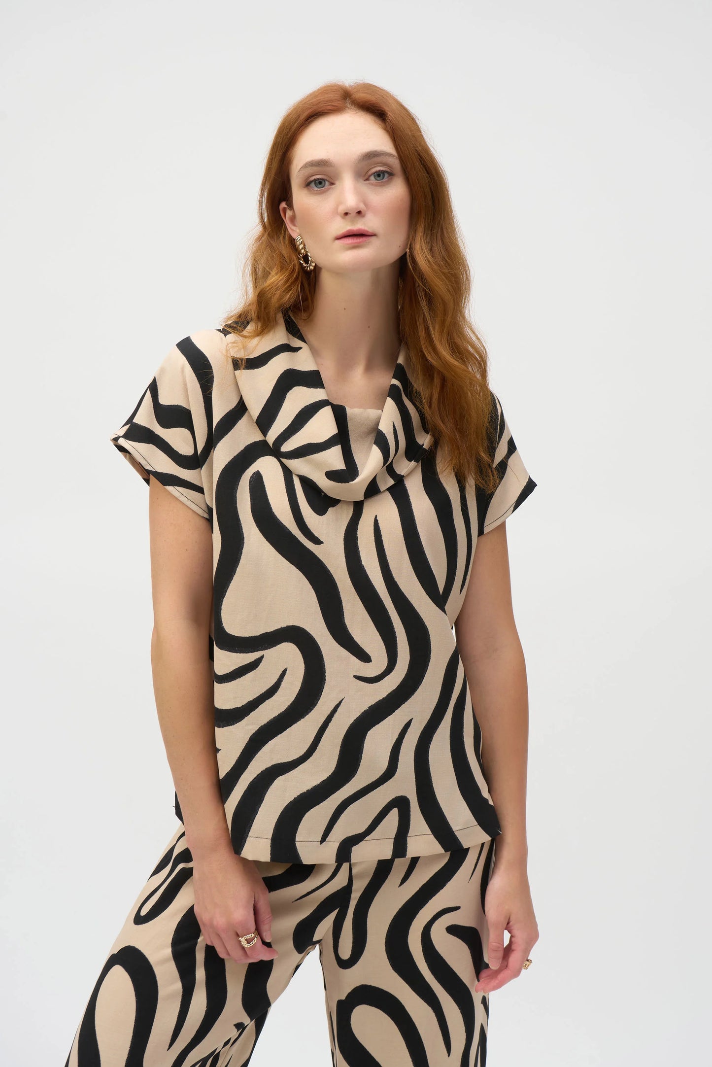 A person with long auburn hair wears a matching outfit featuring a wavy black and beige pattern, including the Gauze Abstract Print Cowl Neck Top 252212 by Joseph Ribkoff. This relaxed-fit top is made from organic cotton and features a draped neckline and short sleeves against a plain white background.