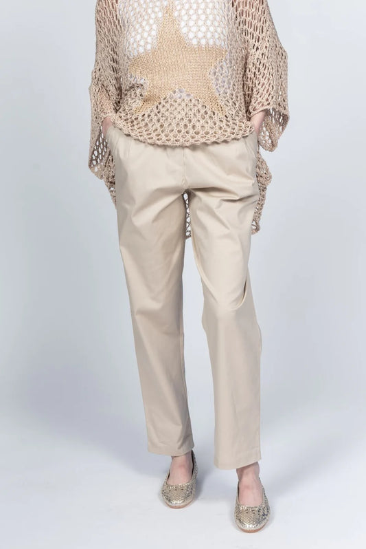 A person wearing Pablo Tricot Pants with Belt LX38551 and a beige mesh sweater featuring a large star design enjoys the comfort of their gold loafers. Made in Italy, this chic ensemble stands out against the light gray background, with hands casually resting in pockets.