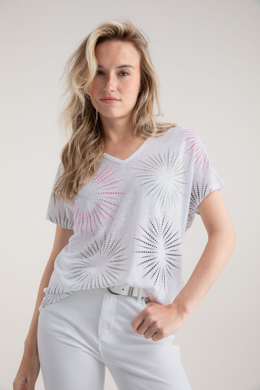 A person with long blonde hair wears the Top T-shirt 7848 MARBLE by MARBLE, featuring a light, relaxed fit and circular perforated pattern, paired with white pants — ideal for everyday wear. They stand against a plain background, gazing at the camera with a neutral expression.