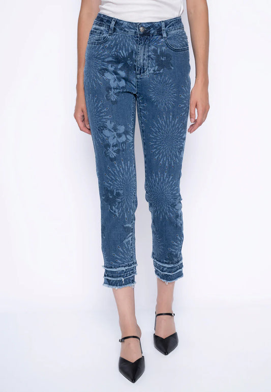 Wearing high-rise Frayed Hem Cropped Jean G6077GX-PICADILLY by Joseph Ribkoff, the individual sports blue jeans with subtle fireworks on a white background. With front pockets, button and zipper closure, and a stretchy design, they stand barefoot with legs slightly apart for comfort.