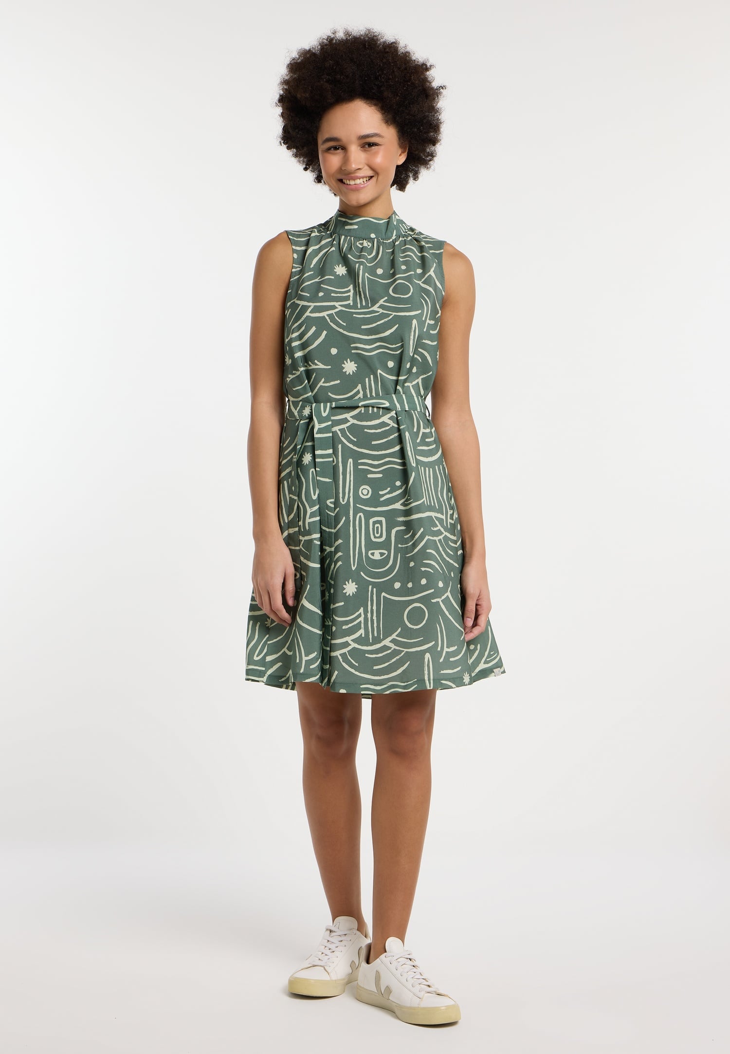 A person models the RAGWEAR ANGYC PRINT DRESS 2511-20030-5033, a green sleeveless vegan dress with abstract white patterns. Against a white background, they smile with curly hair and pair it with white sneakers, highlighting this summer wardrobe essential.